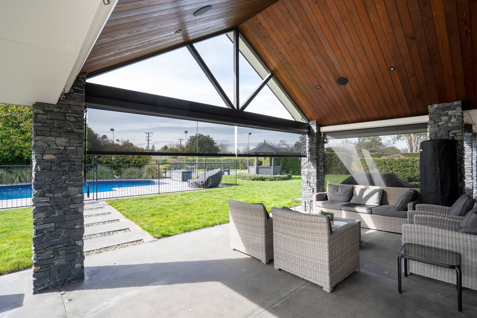 Omni Lite outdoor screen blinds lowered around a cedar-lined pavilion overlooking a pool