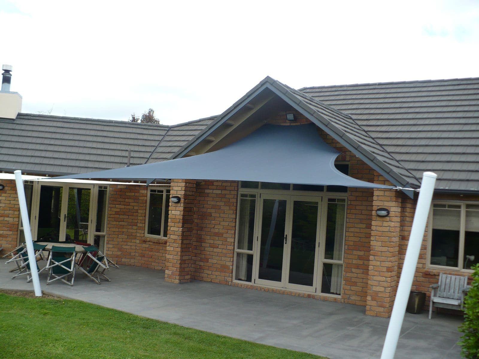 Grey shade sail over a brick home’s patio doors
