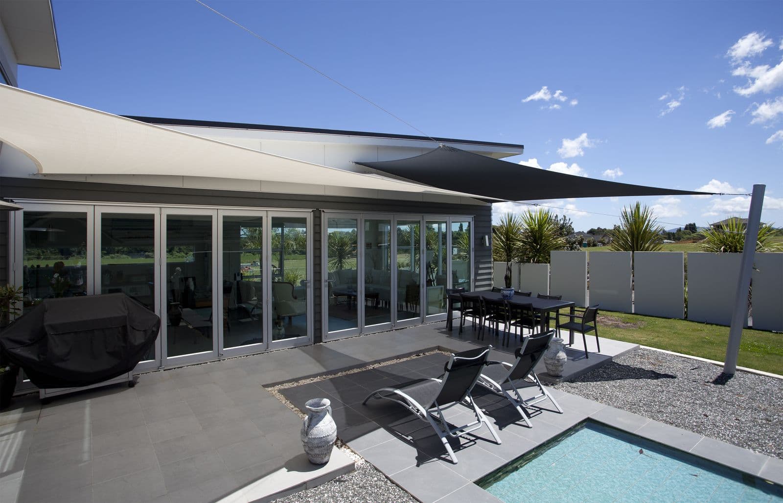 White shade sails over a modern home’s poolside patio