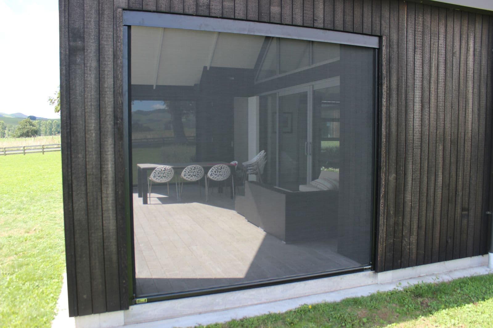 Ziptrak mesh blind on a black-clad home with the lounge beyond