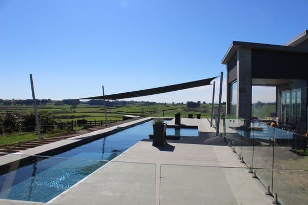 Twin blue shade sails shading a landscaped garden and stone retaining wall