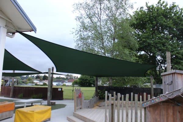 Green shade sail mounted above a timber deck and children's play area