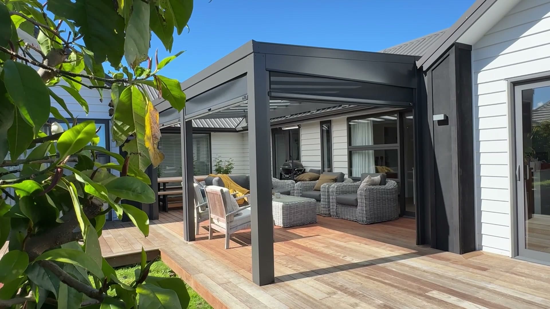 Black Ally-Gola opening-roof pergola over a timber deck with lounge furniture