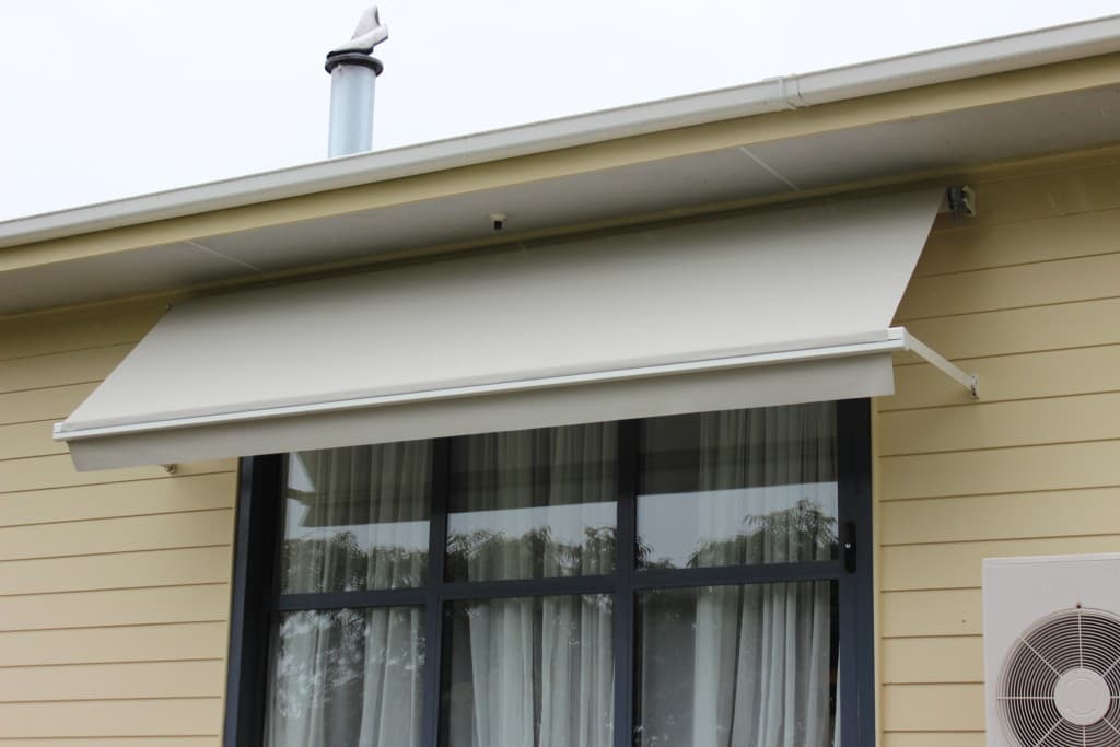 Grey drop arm window awning angled over a home's window
