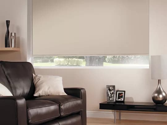 Blockout thermal roller blinds behind a leather armchair