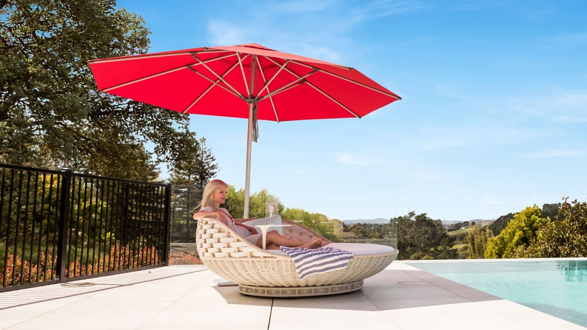 Red Shade7 Milan centre-pole umbrella shading a poolside seating area