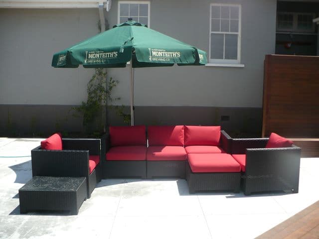 Outdoor furniture reupholstered with red cushions beneath a green umbrella